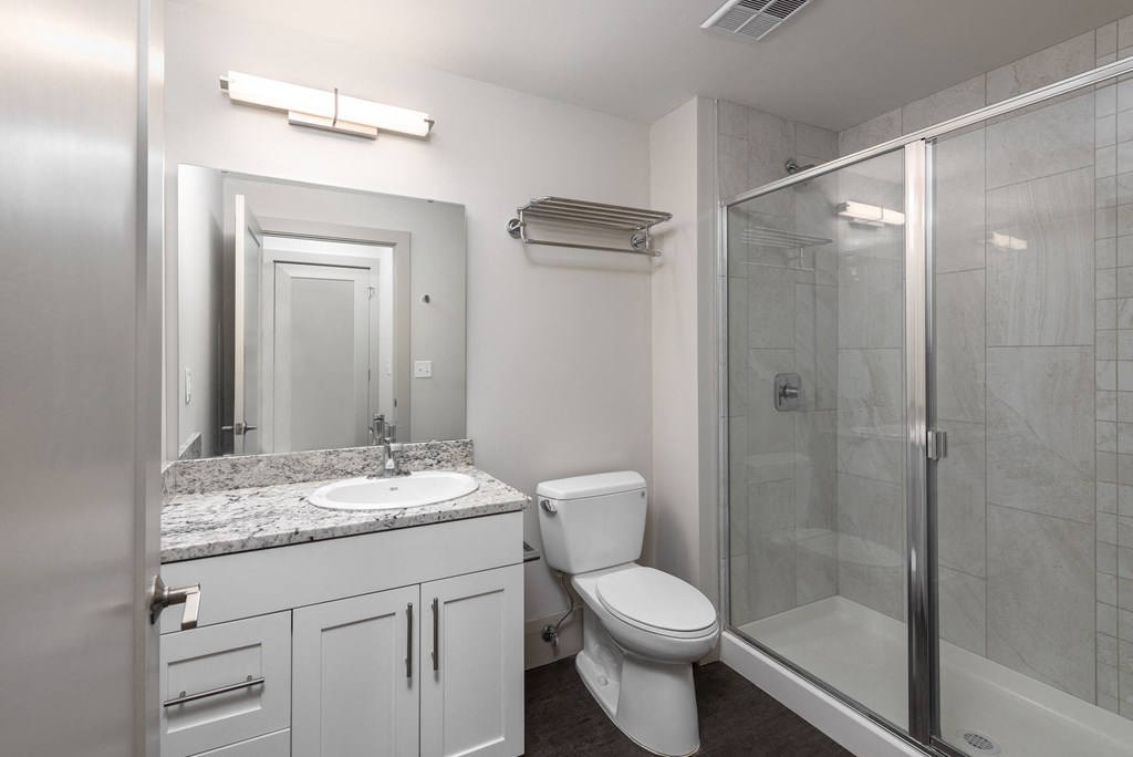 Hibernia bathroom with white cabinets, oversized mirror and sliding glass door shower at Hibernia Apartments, St Louis