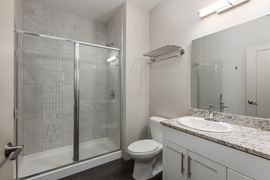 Hibernia bathroom with white cabinets, oversized mirror and sliding glass door shower at Hibernia Apartments, St Louis, MO