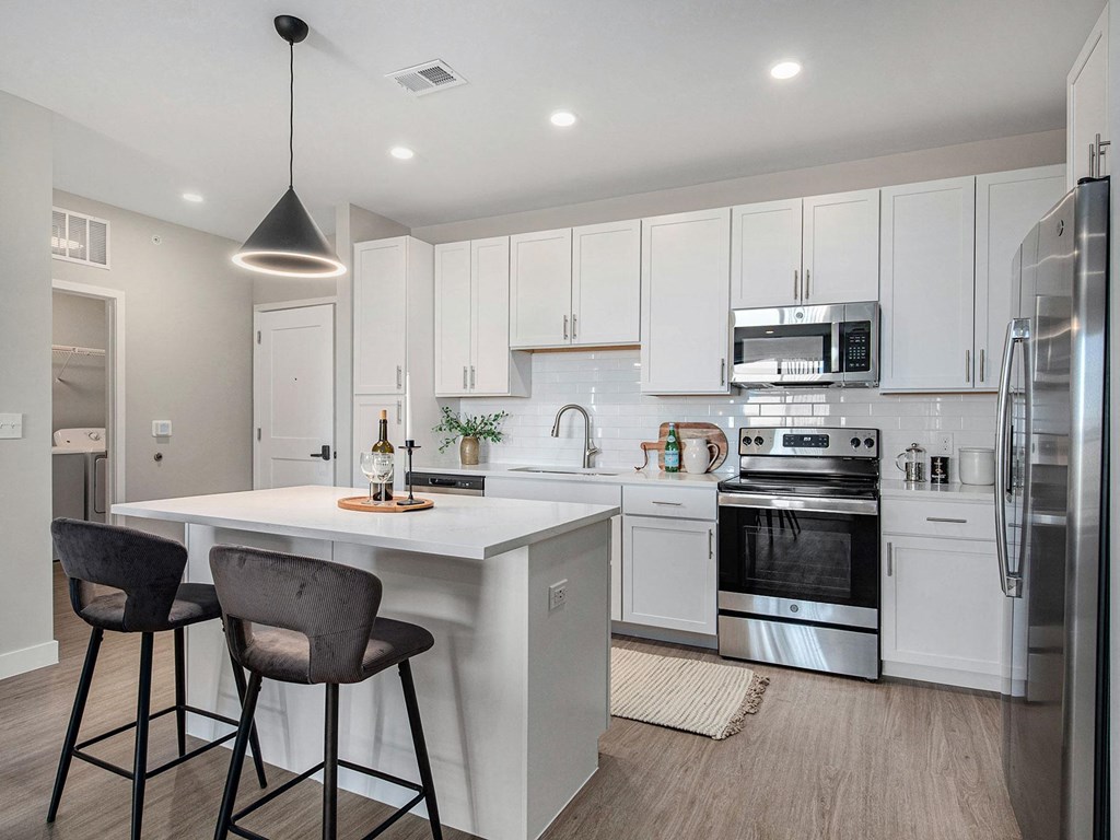a kitchen with white cabinets and a white island with two stools  at Signature at West Pryor, Missouri