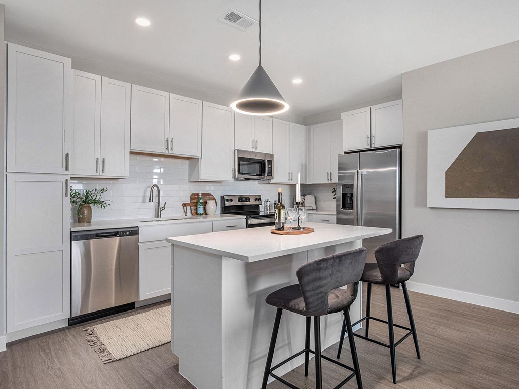 a kitchen with white cabinets and a white island with two stools a kitchen with white cabinets and a white island with two stools at Signature at West Pryor, Lee's Summit, 64081