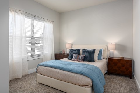 A bedroom with a bed, nightstand, and window with curtains at Hawk Ridge Apartments, Lake St. Louis, MO 