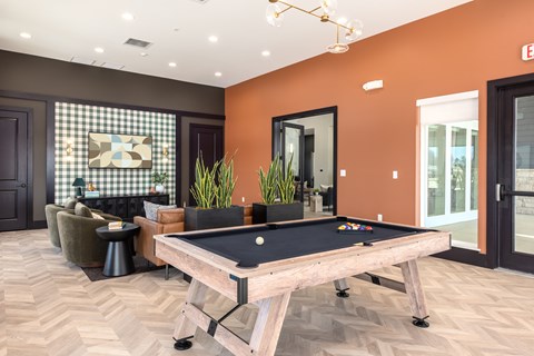 A pool table is in the middle of a room with a brown floor and orange walls at Montage at Hawk Ridge Apartments, Lake St. Louis, 63367, Missouri