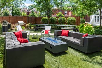 A modern outdoor seating area with grey couches and red cushions.
