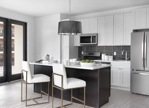 a kitchen with white cabinets and a black island with white chairs