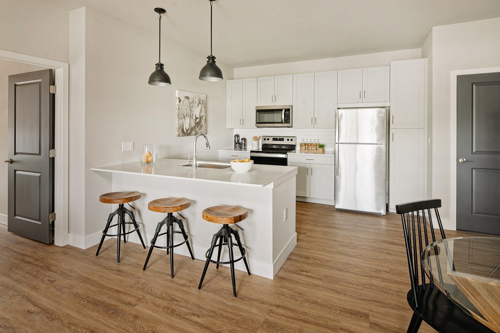 a kitchen with white cabinets and a bar with three stools a kitchen with white cabinets and a bar with three stools at 44 West Luxury Living, Missouri
