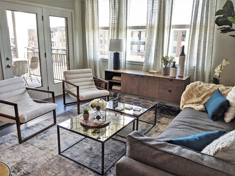 A living room with a grey couch, a glass coffee table, and a white chair.