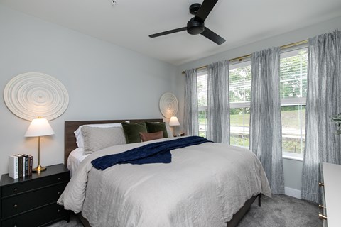 A bedroom with a large bed, a ceiling fan, and a window with curtains at The Cunningham Apartments, West Des Moines, Iowa