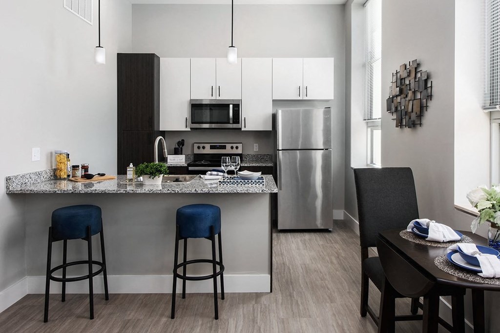 model kitchen with two- tone cabinetry, stainless steel appliances, granite countertops, plank flooring, designer lighting and kitchen island with seating  at The Residences at Delmar DivINe, St Louis