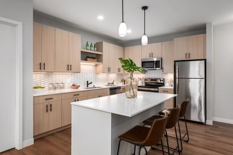 The Flats at Wildhorse Village model kitchen with plank flooring, light colored cabinets, white quartz countertops, stainless steel appliances, large kitchen island with overhang and 3 stools