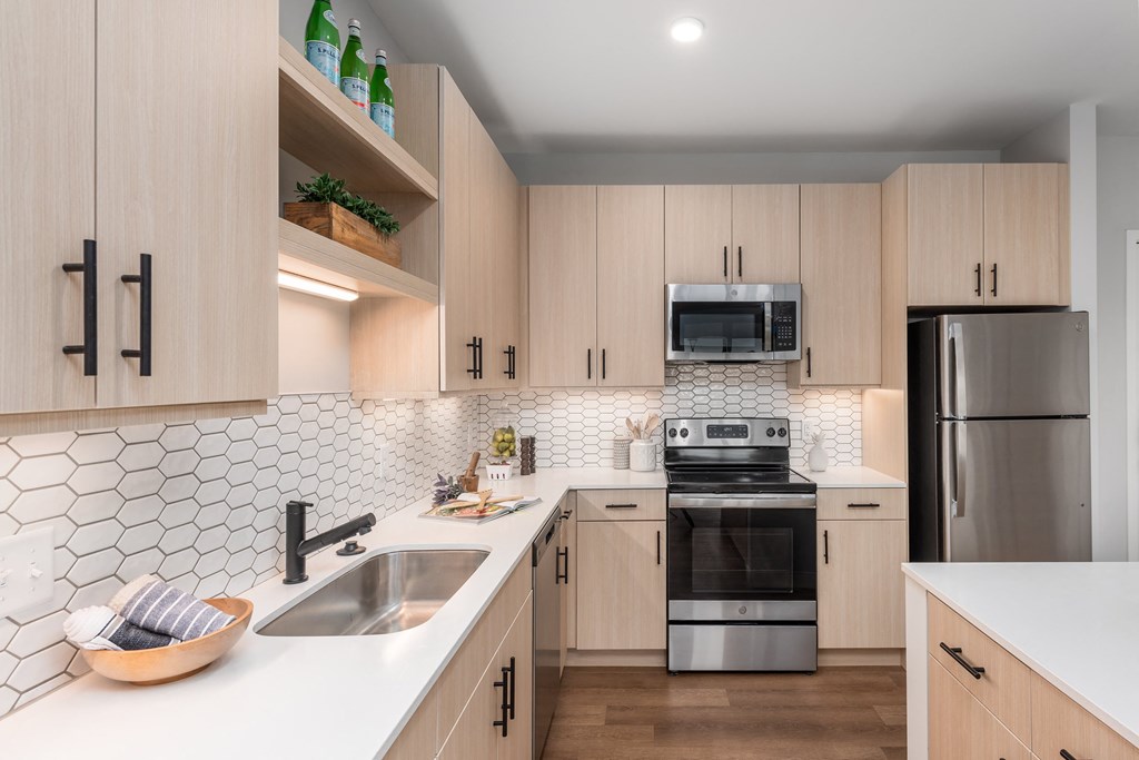 model kitchen with plank flooring, light colored cabinets, white quartz countertops, stainless steel appliances, black finishes and tile backsplash at The Flats & Terraces at Wildhorse Village, Cheste