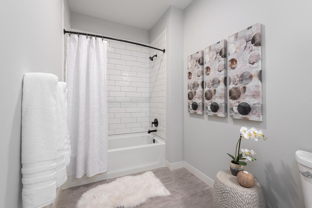 model bathroom with bath tub/shower combo with tile surround and black finishes at The Flats & Terraces at Wildhorse Village, Chesterfield, 63005