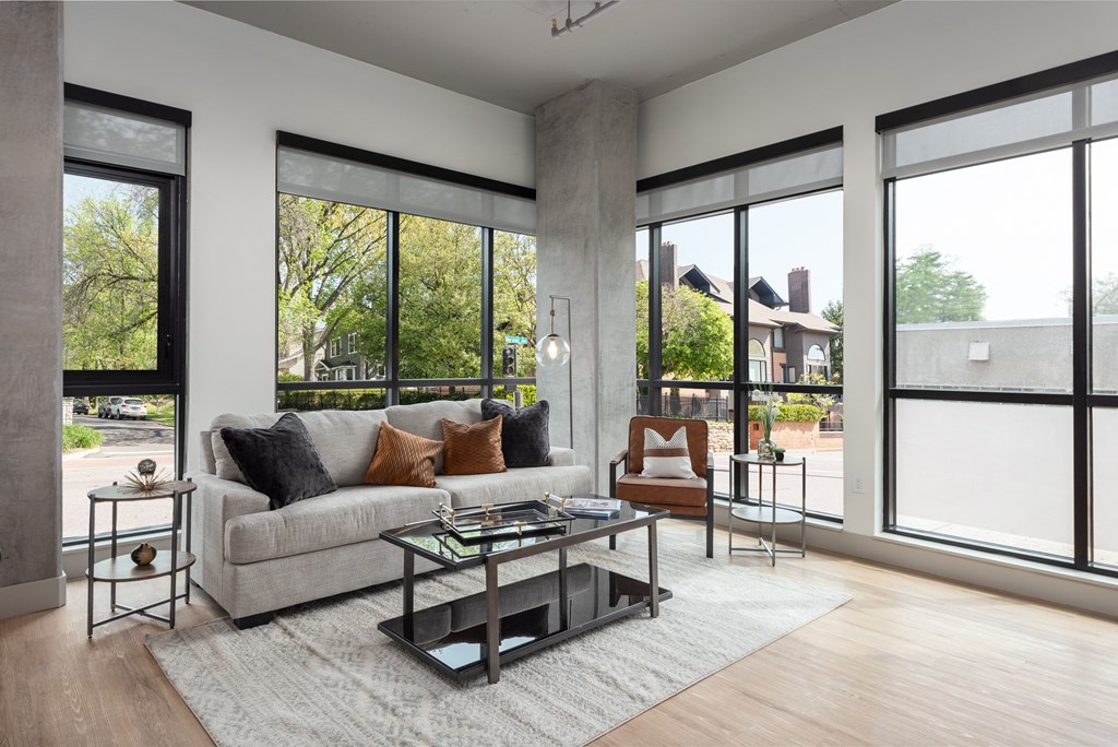 a living room with a couch and a table in front of large windows at Bemiston Place Apartments, Missouri, 63105