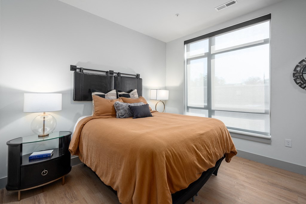 a bedroom with a large window and a bed with an orange blanket and pillows at Bemiston Place Apartments, Missouri, 63105