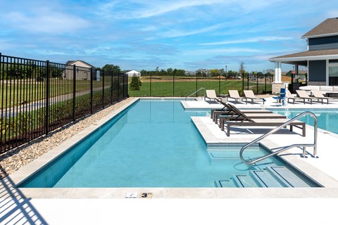 A black fence surrounds a small pool with a few chairs around it.
