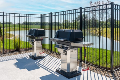 Two barbecue grills are placed on a patio with a view of a lake.