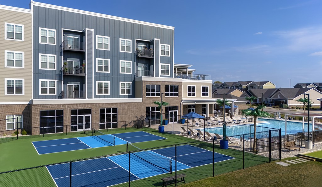 A tennis court is located in front of a large apartment building.