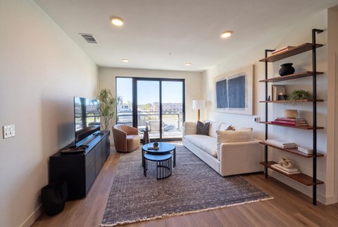 A living room with a white couch, a black coffee table, and a large window with a view of the outside.