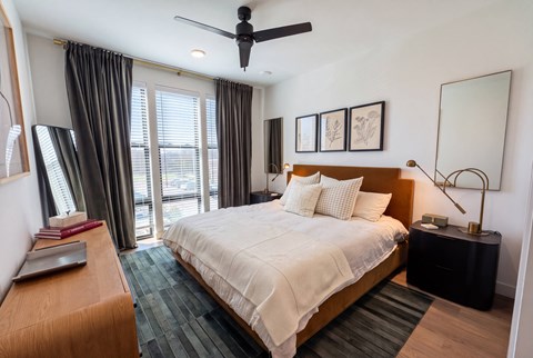 A bedroom with a large bed, a ceiling fan, and a window with curtains.