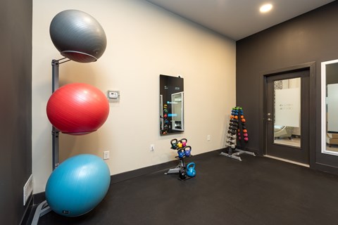 A room with a blue exercise ball, a red exercise ball, a grey exercise ball, and a pair of blue dumbbells.