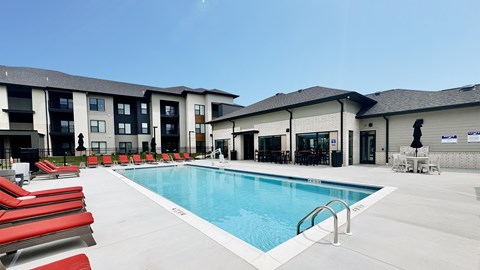 A swimming pool with red lounge chairs and a building in the background.