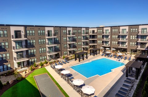 A large swimming pool is surrounded by sun loungers in front of apartment buildings. at The Cunningham Apartments, Apartments, West Des Moines, IA