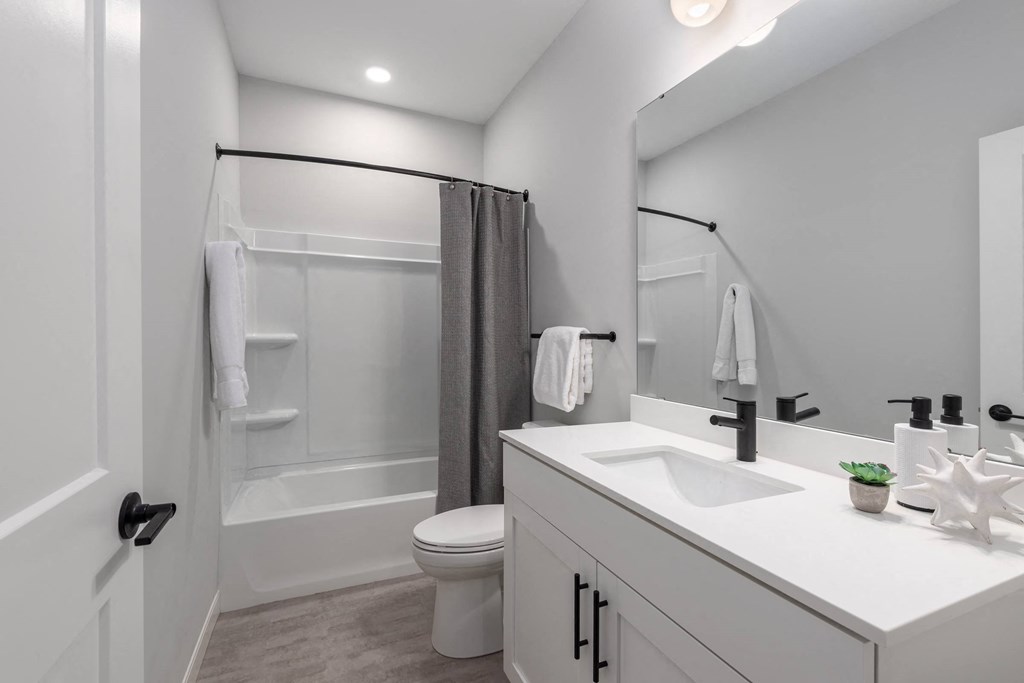 2nd bathroom with tub, white quartz vanity, modern white cabinetry, matte black finishes and large mirror at The Flats & Terraces at Wildhorse Village, Chesterfield Missouri