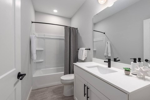 2nd bathroom with tub, white quartz vanity, modern white cabinetry, matte black finishes and large mirror at The Flats & Terraces at Wildhorse Village, Chesterfield Missouri
