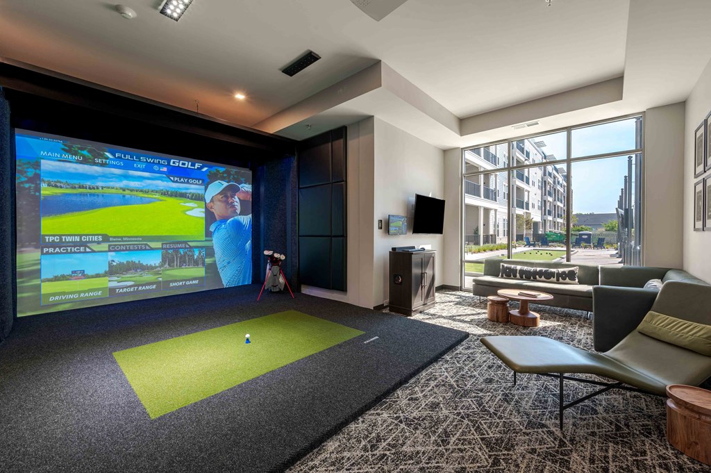 A room with a golf simulator and a couch.