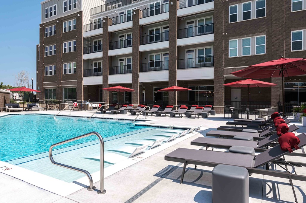 A large swimming pool surrounded by red sunshades and lounge chairs.