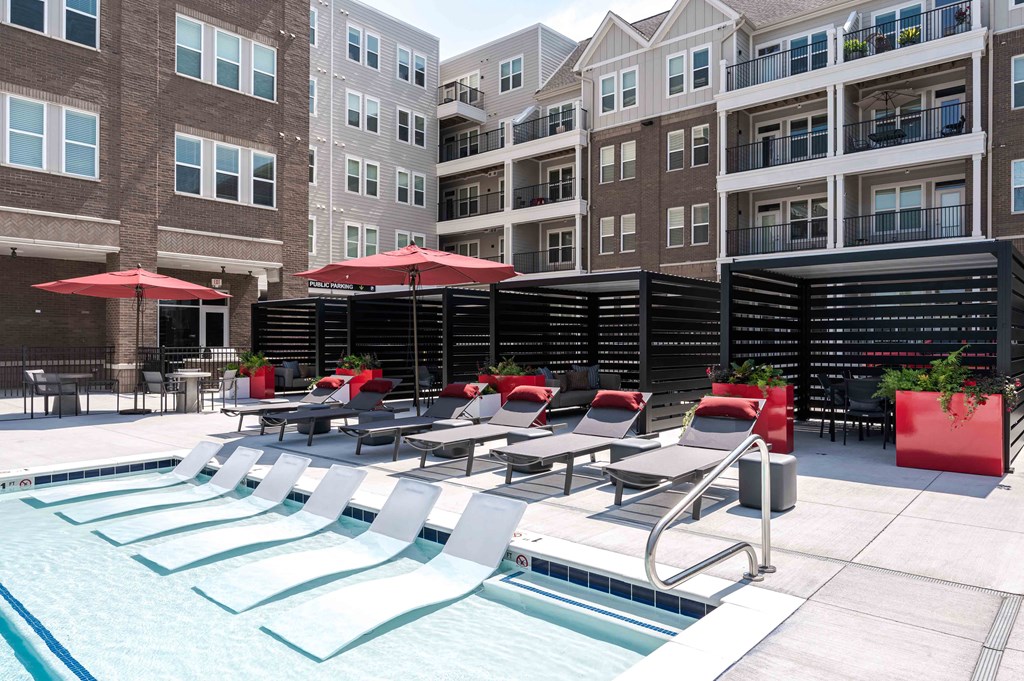 A pool area with red umbrellas and lounge chairs.