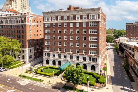 A large red brick building with a green awning sits in the middle of a city street.