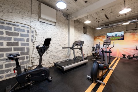 A gym with exercise equipment and a TV screen showing a sunset.