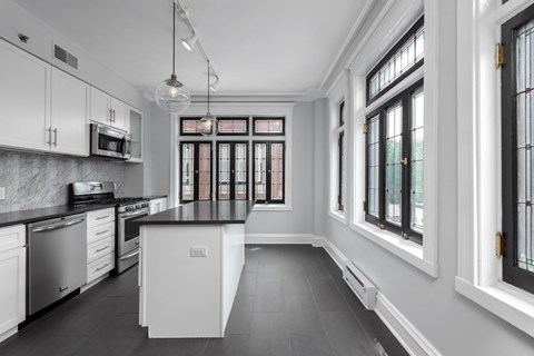 York House designer kitchen with gas stove, quartz countertops, stainless steel appliances, marble kitchen backsplash, and slate tile floor. Oversized windows, large kitchen island and soft close cabinetry.