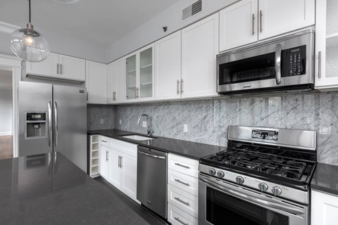 York House designer kitchen with gas stove, quartz countertops, stainless steel appliances, marble kitchen backsplash, and slate tile floor. Oversized windows, large kitchen island and soft close cabinetry.