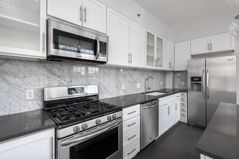 York House designer kitchen with gas stove, quartz countertops, stainless steel appliances, marble kitchen backsplash, and slate tile floor. Oversized windows, large kitchen island and soft close cabinetry.