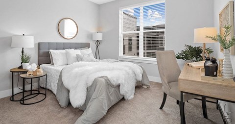 A bedroom with a grey bedspread and a round mirror on the wall.