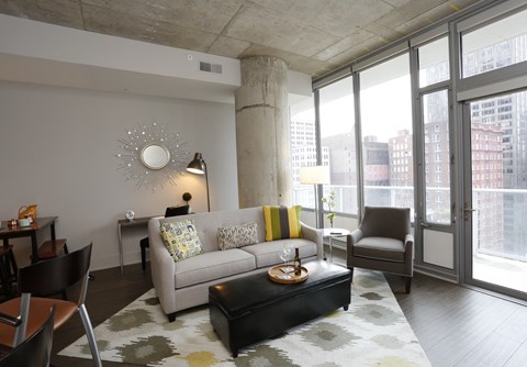 A living room with a grey couch, a coffee table, and a large window.