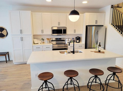 a kitchen with white cabinets and a white island with four wooden stools