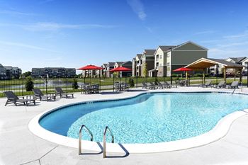 a pool with chairs and umbrellas in front of apartment buildings at Thirteen01 at Hartman Lakes, Shiloh, Illinois