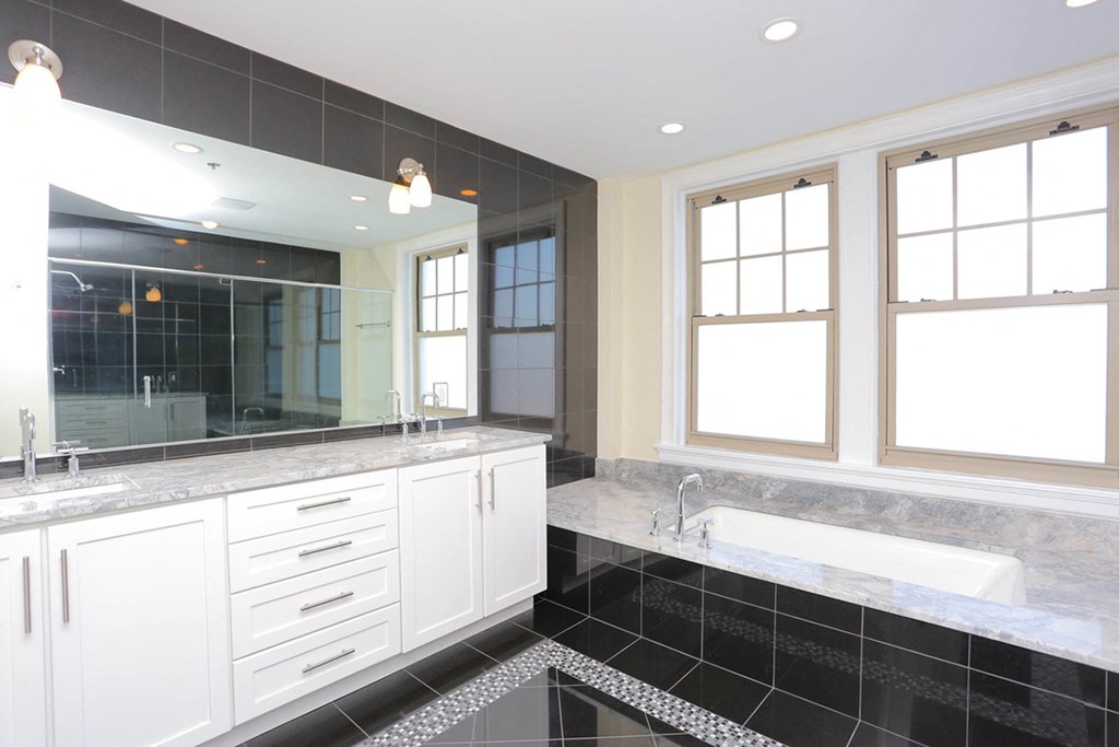 Penthouse bathroom with set in bathtub surrounded by dark tile, white vanity and mirror at York House, Saint Louis, Missouri