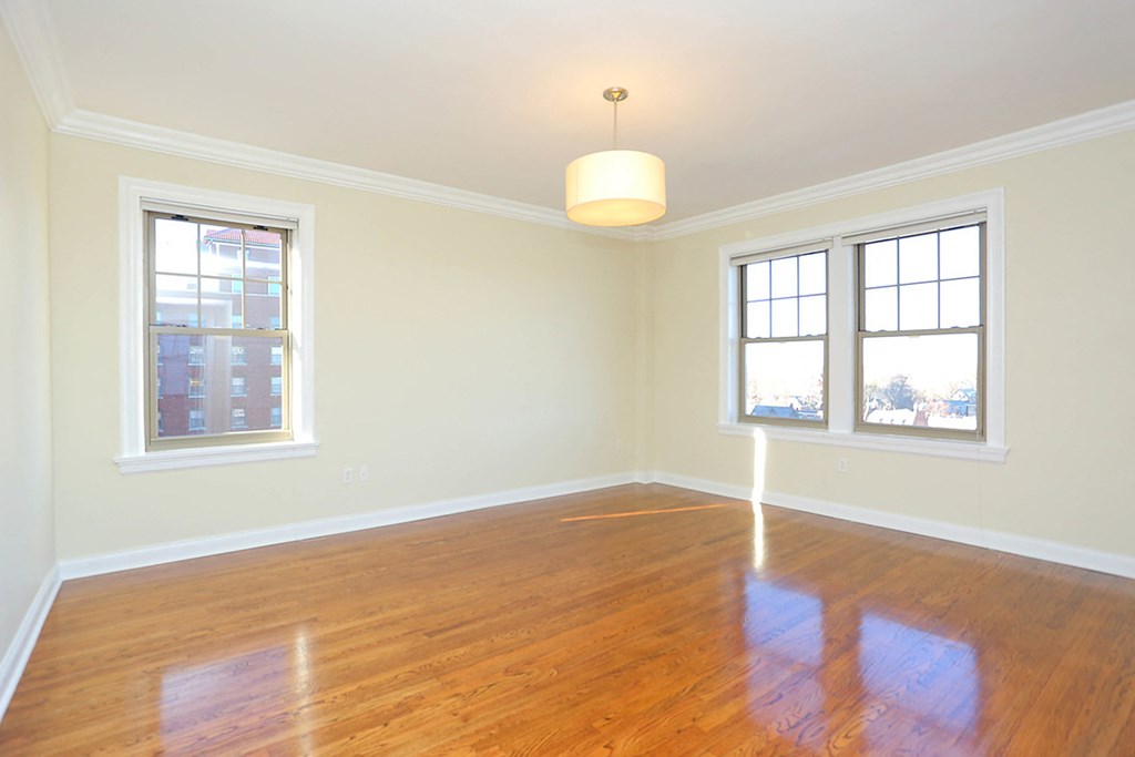 bedroom with light wood flooring, three windows, and ceiling light with shade. at York House, Saint Louis, 63108