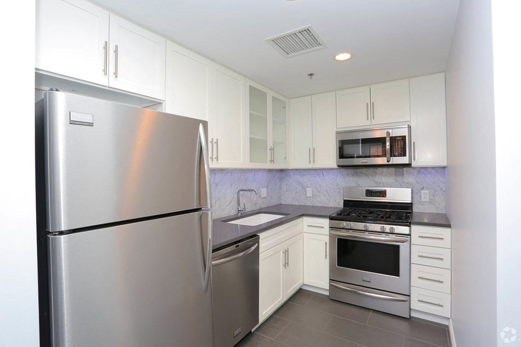 York House kitchen with stainless steel refrigerator, dishwasher, stove and microwave, white cabinets and granite backsplash and countertops. at York House, Saint Louis, Missouri
