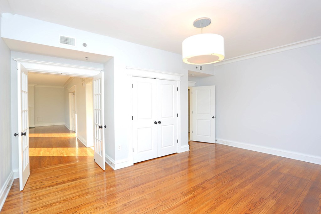 Living room with light wood flooring, white walls, front door and overhead light with shade. at York House, Saint Louis, Missouri