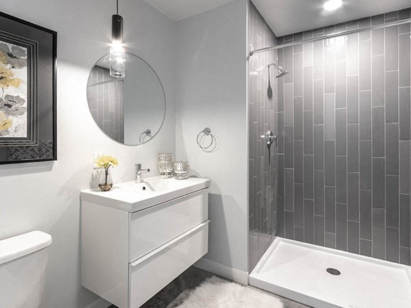Steelcote Crossing bathroom with white cabinetry, white quartz countertops, large circular mirror and walk in shower with tile surround at Steelcote Square, Missouri