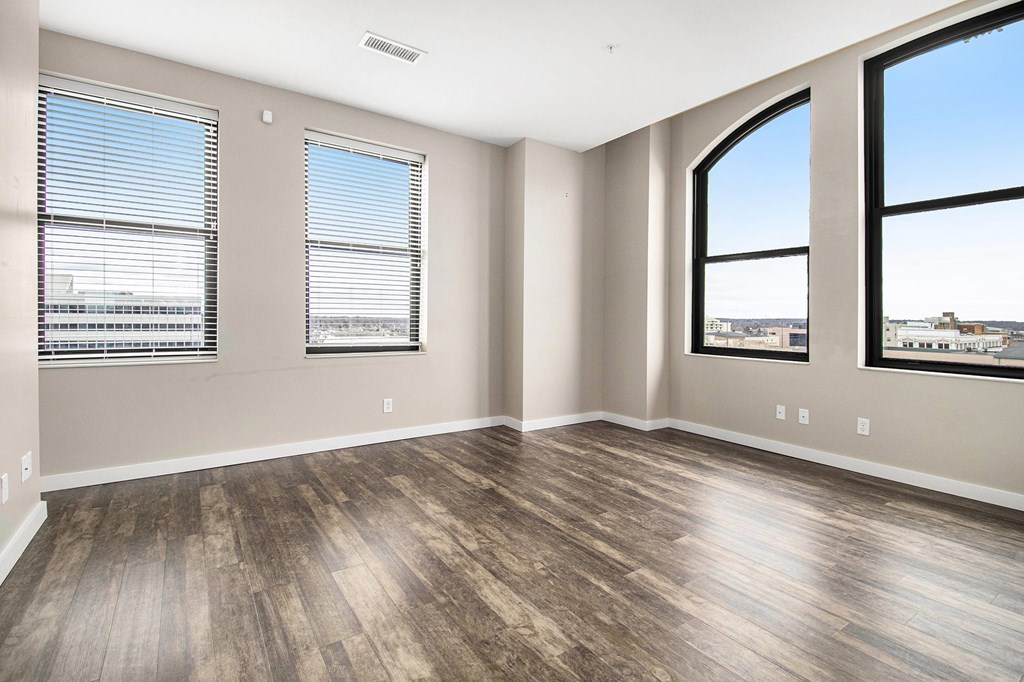A room with wooden flooring and two windows.