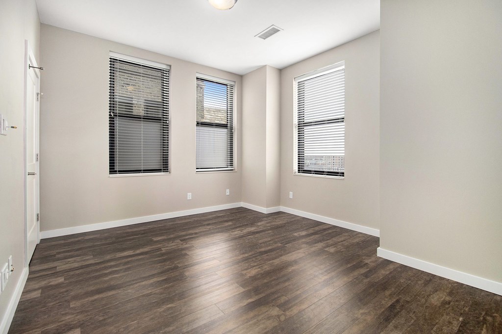 A room with wooden flooring and two windows with blinds.