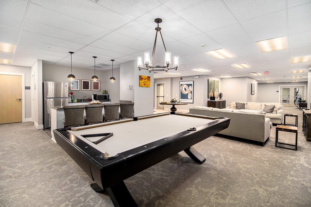 A pool table is in the middle of a room with a couch and a fridge in the background.