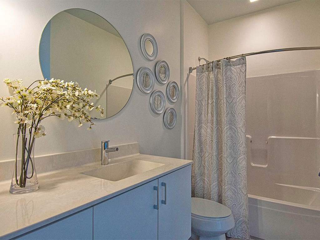 Steelcote Lofts bathroom with white cabinetry and white quartz countertops. Large circular mirror and tile at Steelcote Square, St. Louis, 63103