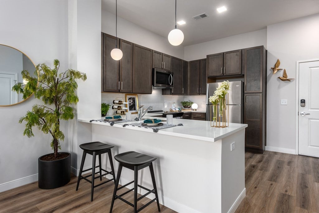 Modern kitchen with designer lighting, quartz countertops, dark cabinetry and stainless steel appliances  with countertop with seating  at Chapter at the Streets of St Charles, Saint Charles, 63303