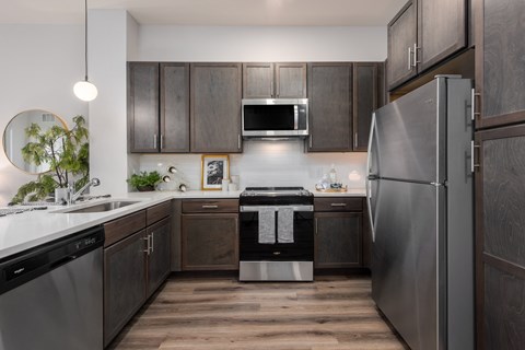 Modern kitchen with designer lighting, quartz countertops, dark cabinetry and stainless steel appliances  at Chapter at the Streets of St Charles, Saint Charles, MO